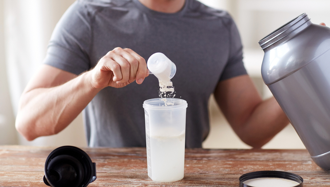 man scooping protein powder into drink